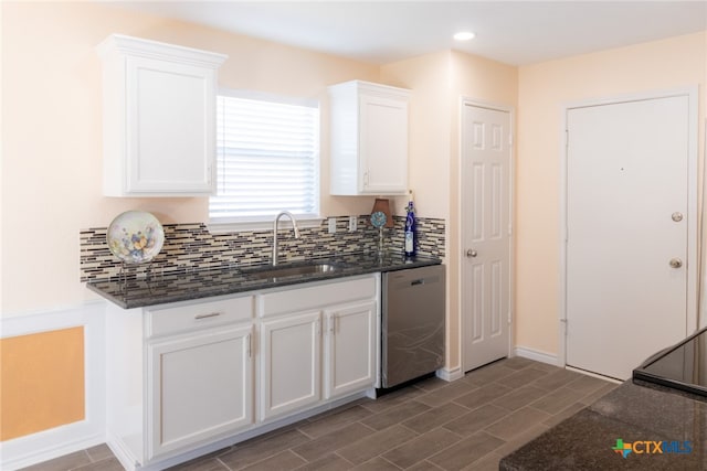 kitchen featuring white cabinetry, backsplash, sink, dark stone countertops, and stainless steel dishwasher