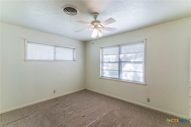 carpeted spare room featuring baseboards, ceiling fan, visible vents, and plenty of natural light