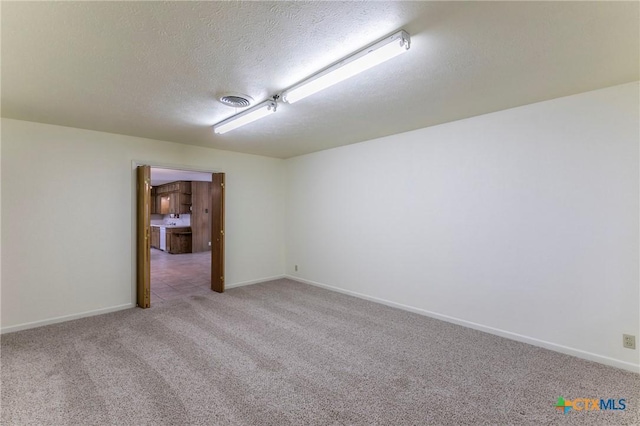 spare room featuring light colored carpet, visible vents, baseboards, and a textured ceiling