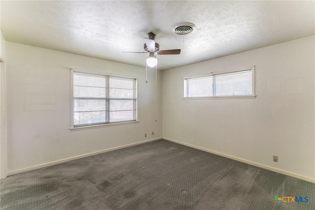 unfurnished room with a textured ceiling, visible vents, baseboards, ceiling fan, and dark colored carpet