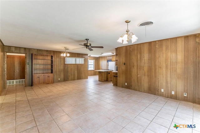 spare room featuring light tile patterned floors, visible vents, wooden walls, and ceiling fan with notable chandelier