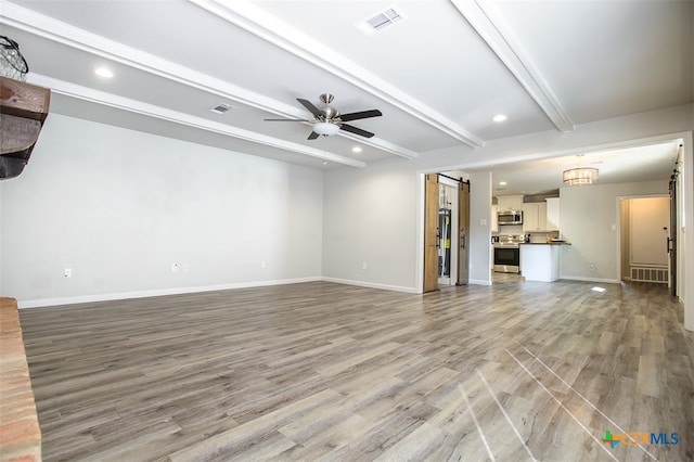 unfurnished living room featuring light hardwood / wood-style floors, beamed ceiling, a barn door, and ceiling fan