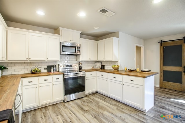 kitchen featuring stainless steel appliances, wooden counters, a barn door, and white cabinetry