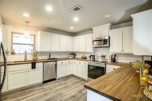 kitchen featuring butcher block counters, stainless steel appliances, white cabinetry, sink, and pendant lighting