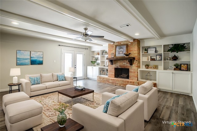 living room with french doors, beam ceiling, a brick fireplace, dark wood-type flooring, and ceiling fan