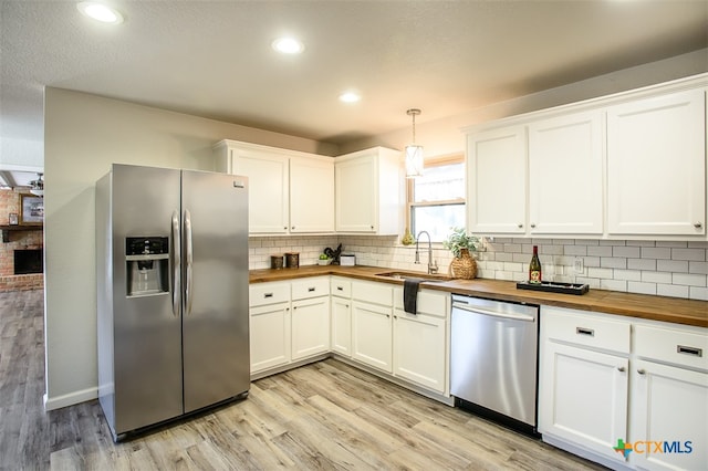 kitchen with butcher block counters, appliances with stainless steel finishes, hanging light fixtures, light hardwood / wood-style floors, and white cabinets