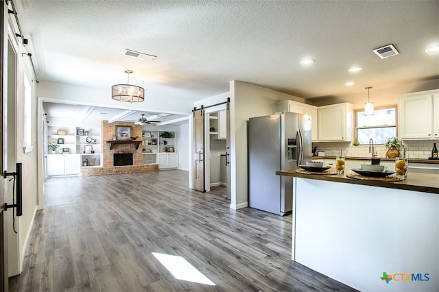 kitchen with wood-type flooring, a barn door, pendant lighting, stainless steel refrigerator with ice dispenser, and white cabinets