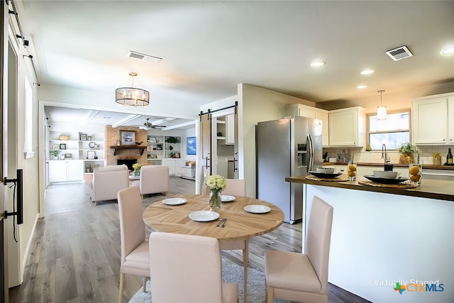 dining space featuring built in shelves, hardwood / wood-style floors, a barn door, beamed ceiling, and ceiling fan