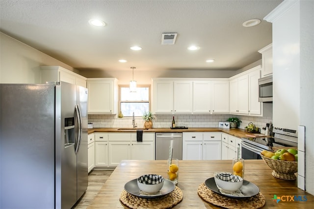 kitchen featuring stainless steel appliances, white cabinetry, wood counters, pendant lighting, and decorative backsplash