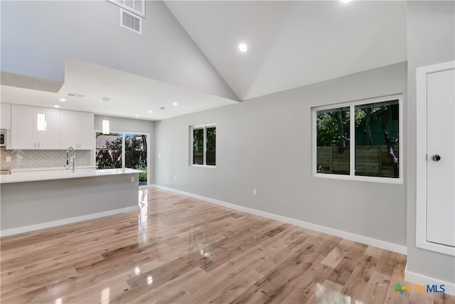 unfurnished living room with light wood-type flooring, sink, and high vaulted ceiling