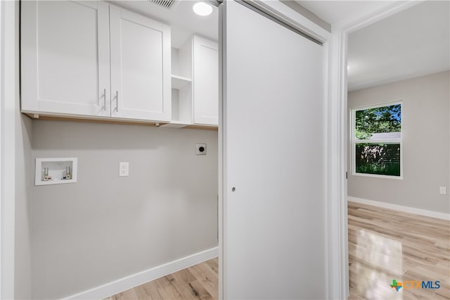 washroom featuring electric dryer hookup, hookup for a washing machine, cabinets, and light wood-type flooring