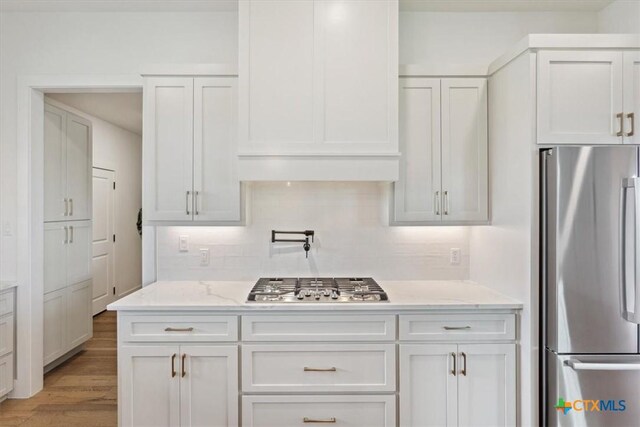 127 Cumberland Dr, Belton, TX 76513 - kitchen featuring appliances with stainless steel finishes, white cabinetry, decorative backsplash, light wood-style flooring, and light stone countertops