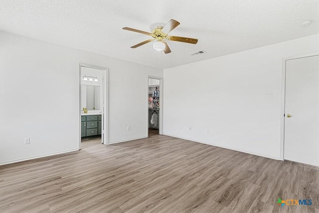 unfurnished bedroom with light wood-type flooring, ceiling fan, a textured ceiling, a walk in closet, and ensuite bathroom