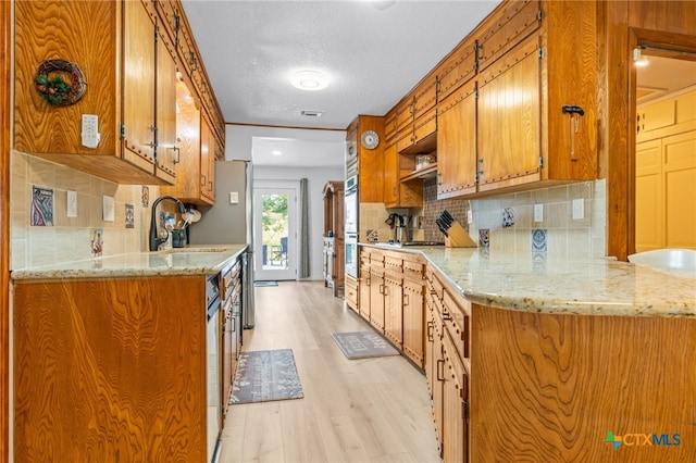 kitchen featuring sink, kitchen peninsula, light stone countertops, backsplash, and light wood-type flooring