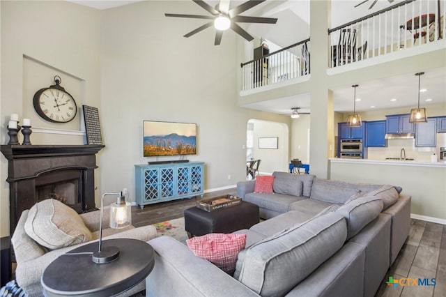 2604 Whitehurst Dr, Round Rock, TX 78681 - living room featuring dark wood finished floors, a ceiling fan, arched walkways, a towering ceiling, and a fireplace
