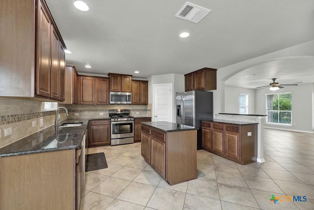 kitchen with a kitchen island, sink, dark stone countertops, backsplash, and stainless steel appliances