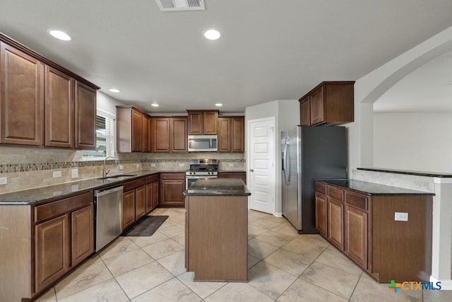 kitchen featuring appliances with stainless steel finishes, sink, backsplash, dark stone counters, and a center island