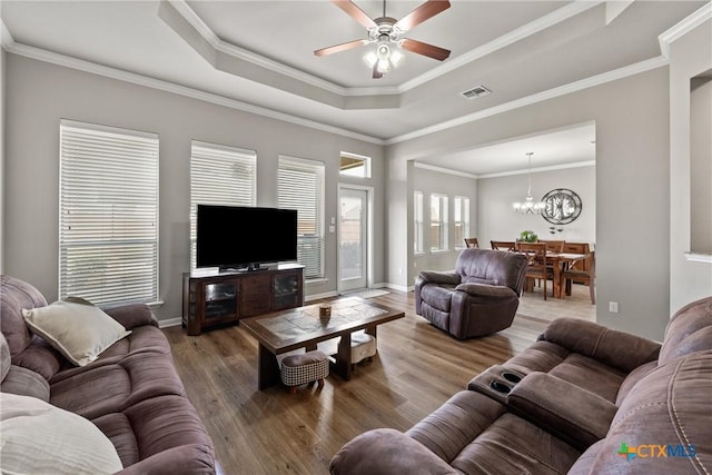 living room with a raised ceiling, visible vents, wood finished floors, baseboards, and ceiling fan with notable chandelier