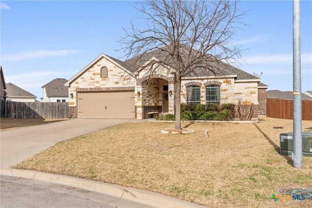 french country home featuring brick siding, concrete driveway, an attached garage, fence, and stone siding