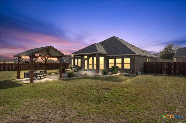 back of house at dusk with a lawn, fence, a gazebo, a patio area, and brick siding