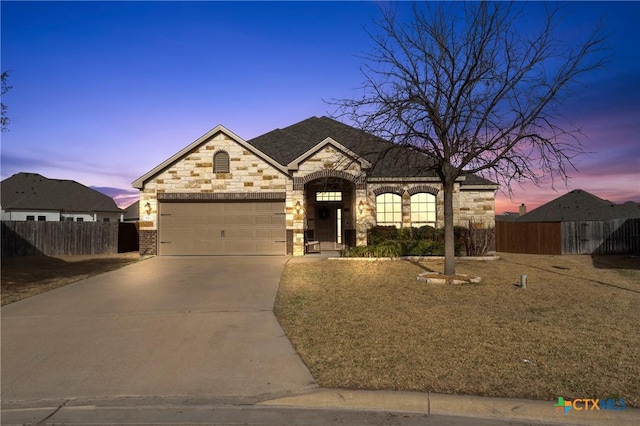 french country style house with driveway, a garage, stone siding, fence, and brick siding