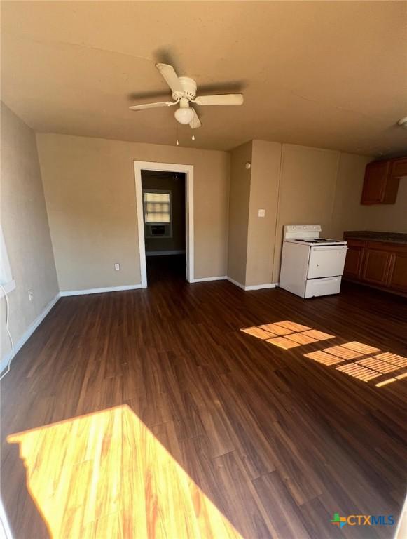unfurnished living room featuring a ceiling fan, baseboards, and dark wood-style flooring