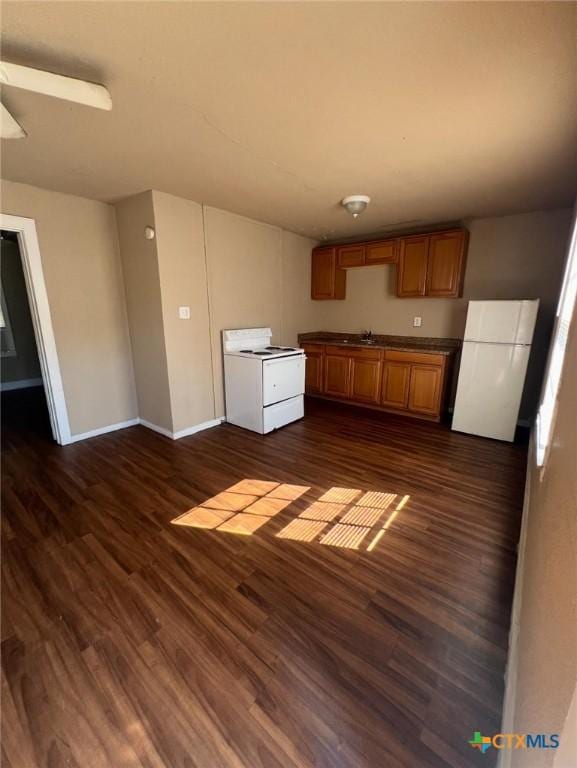 kitchen featuring a sink, dark wood-style flooring, baseboards, white appliances, and brown cabinetry