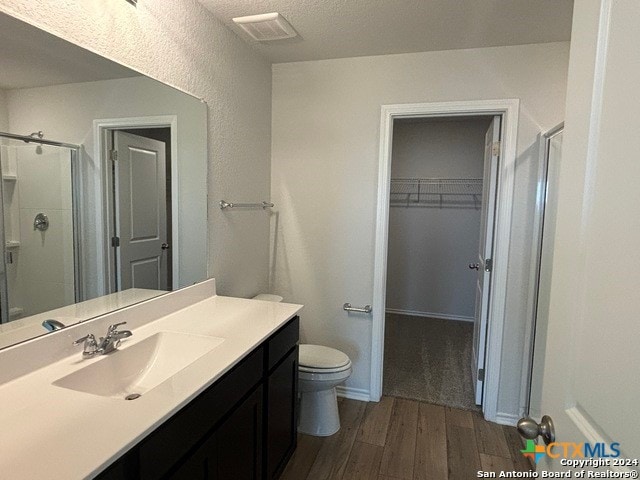 bathroom with toilet, a textured ceiling, hardwood / wood-style flooring, vanity, and walk in shower