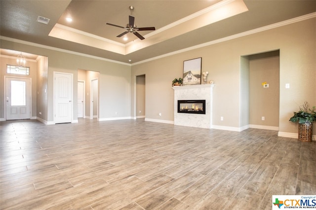 unfurnished living room with a raised ceiling, hardwood / wood-style flooring, ceiling fan, and crown molding