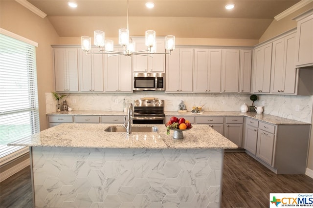 kitchen with lofted ceiling, a center island with sink, light stone countertops, pendant lighting, and appliances with stainless steel finishes