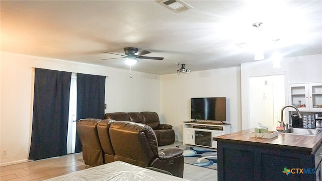 living room featuring ceiling fan, sink, and light wood-type flooring