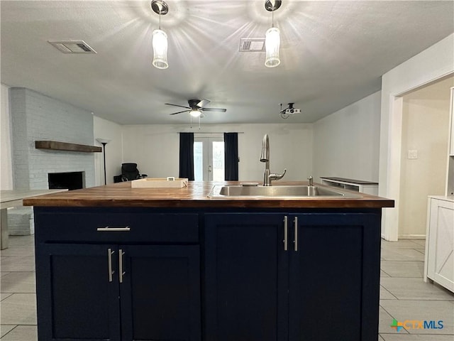 kitchen featuring wood counters, a large fireplace, blue cabinets, sink, and an island with sink