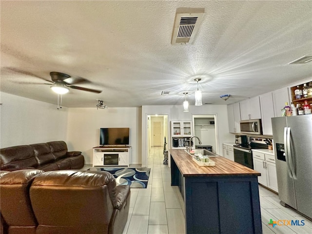 kitchen featuring white cabinets, appliances with stainless steel finishes, a center island with sink, and hanging light fixtures