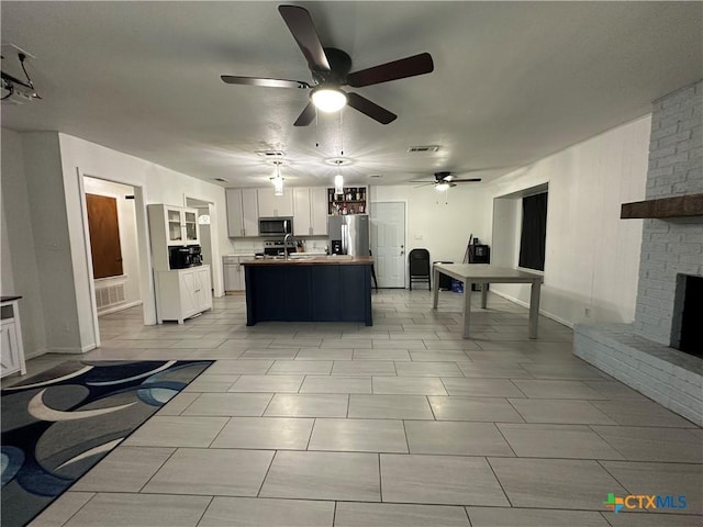 kitchen featuring a center island, white cabinets, a brick fireplace, ceiling fan, and appliances with stainless steel finishes