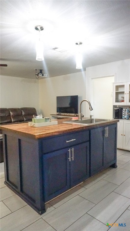 kitchen with a kitchen island with sink, blue cabinets, sink, white cabinetry, and butcher block counters