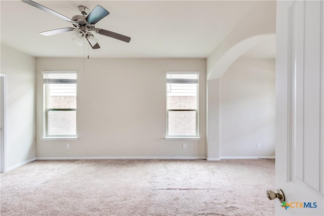 unfurnished room with carpet floors, arched walkways, ceiling fan, and baseboards