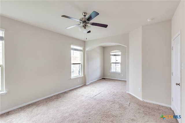 carpeted empty room with arched walkways, a ceiling fan, and baseboards