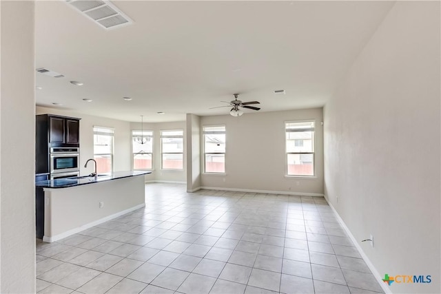 unfurnished living room with a ceiling fan, light tile patterned flooring, baseboards, and a sink