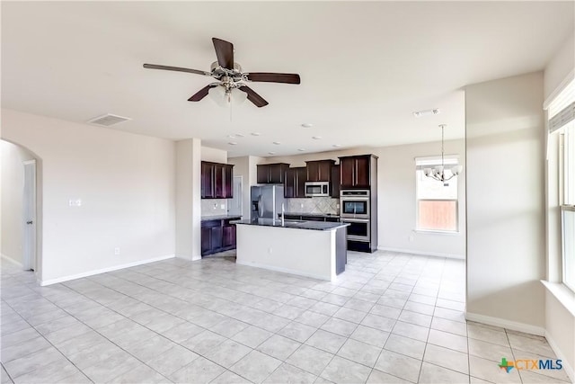 kitchen featuring stainless steel appliances, backsplash, light tile patterned floors, dark countertops, and arched walkways