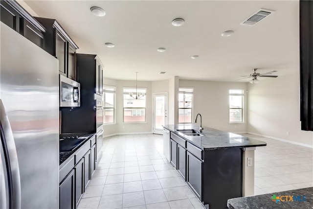 kitchen featuring appliances with stainless steel finishes, a sink, light tile patterned flooring, baseboards, and dark cabinets