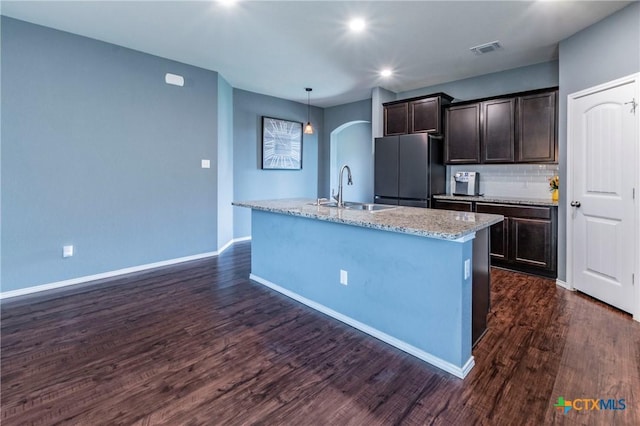 kitchen with a center island with sink, sink, dark brown cabinets, and stainless steel refrigerator