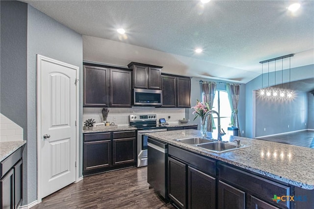 kitchen with appliances with stainless steel finishes, pendant lighting, dark hardwood / wood-style flooring, sink, and a kitchen island with sink