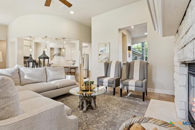 living room with lofted ceiling, ceiling fan, and a stone fireplace