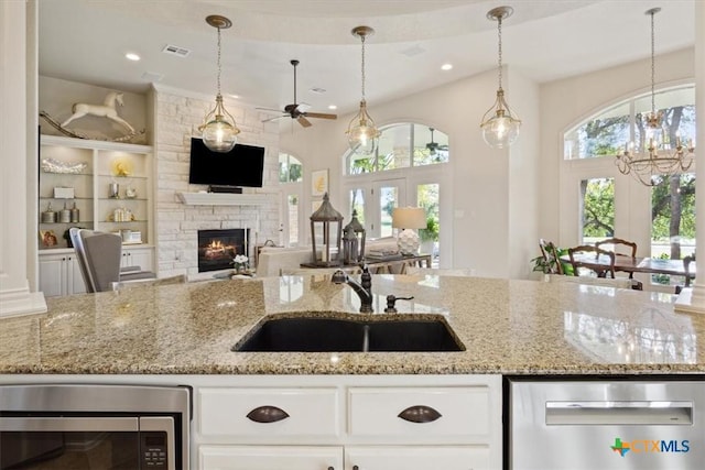 kitchen with sink, appliances with stainless steel finishes, light stone counters, ceiling fan, and a stone fireplace