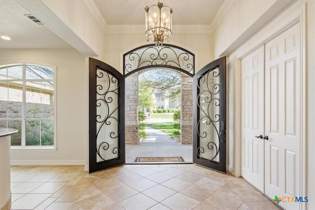 entryway with light tile patterned floors, baseboards, visible vents, crown molding, and a chandelier