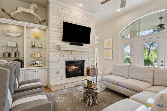 living room featuring ceiling fan, crown molding, and a stone fireplace