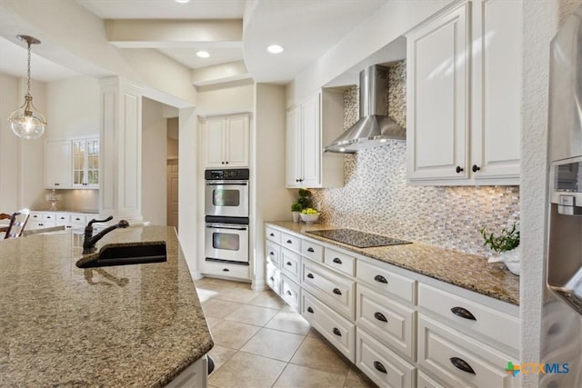 kitchen featuring wall chimney exhaust hood, black electric stovetop, double oven, white cabinets, and dark stone countertops