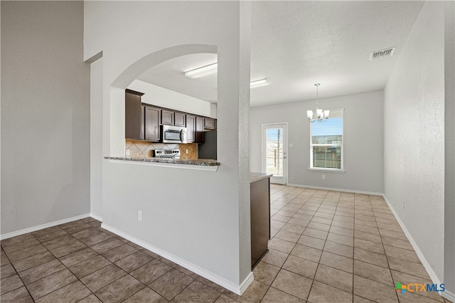 kitchen featuring decorative backsplash, light stone countertops, dark brown cabinets, a notable chandelier, and light tile patterned flooring