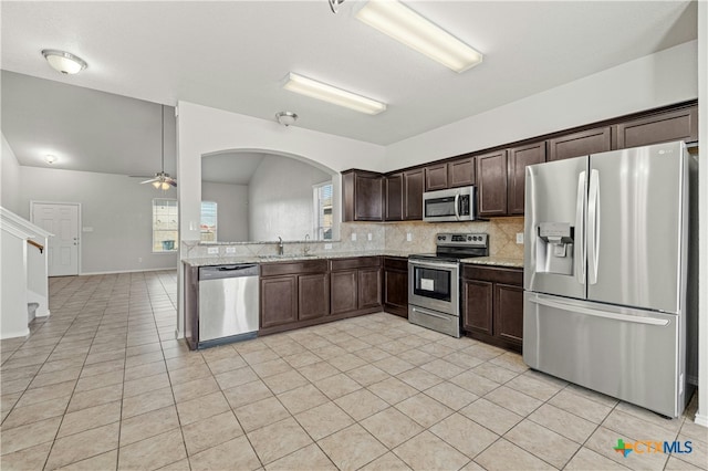 kitchen featuring dark brown cabinetry, light stone counters, vaulted ceiling, light tile patterned floors, and appliances with stainless steel finishes