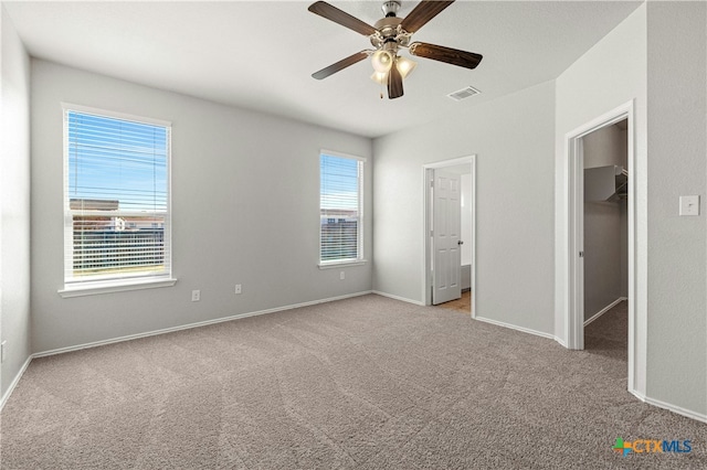 unfurnished bedroom featuring multiple windows, light carpet, ceiling fan, and a walk in closet